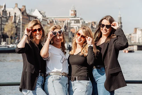 quatre amies souriantes avec des lunettes en forme de cœur posent à amsterdam pendant un jeu de piste evjf paranormal
