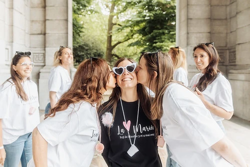 future mariée souriante avec des lunettes en forme de cœur embrassée par deux amies