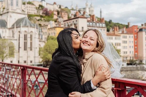 future mariee souriante embrassee par une amie sur une passerelle a lyon pendant le jeu de piste evjf paranormal lyon