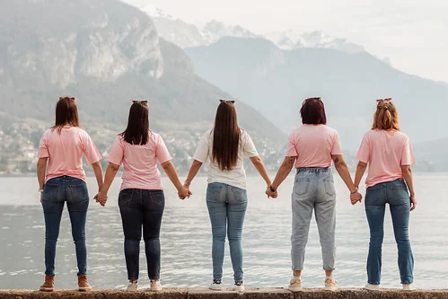 Cinq filles de dos tenant leurs mains face au lac dans une ambiance koh lanta evjf annecy