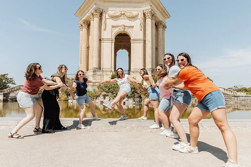 groupe de femmes en evjf koh lanta a montpellier jouant devant un monument avec une participante tiree en riant