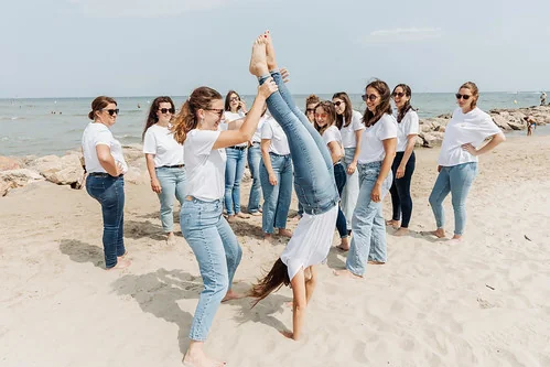 groupe de femmes sur la plage avec une participante faisant un équilibre accompagnee