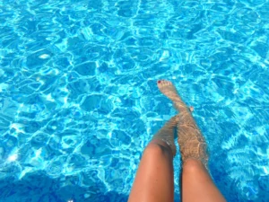 Jambes d’une femme se relaxant dans une piscine bleue sous le soleil