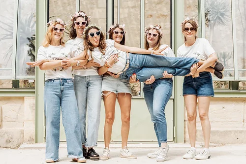 groupe de femmes célébrant un evjf à montpellier posant joyeusement devant une verrière en pierre claire