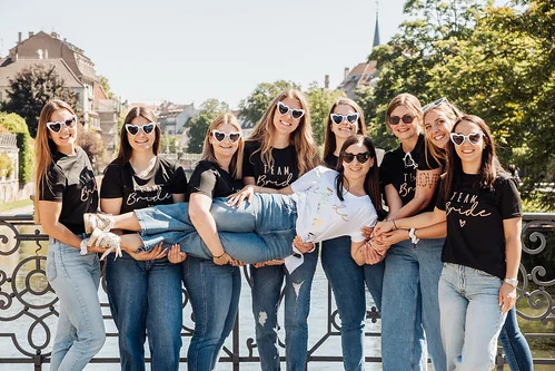 la future mariée portée par ses amies lors du rallye des copines city game evjf à strasbourg sur un pont ensoleillé