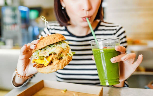 femme mangeant un burger vegetal et buvant un smoothie vert 