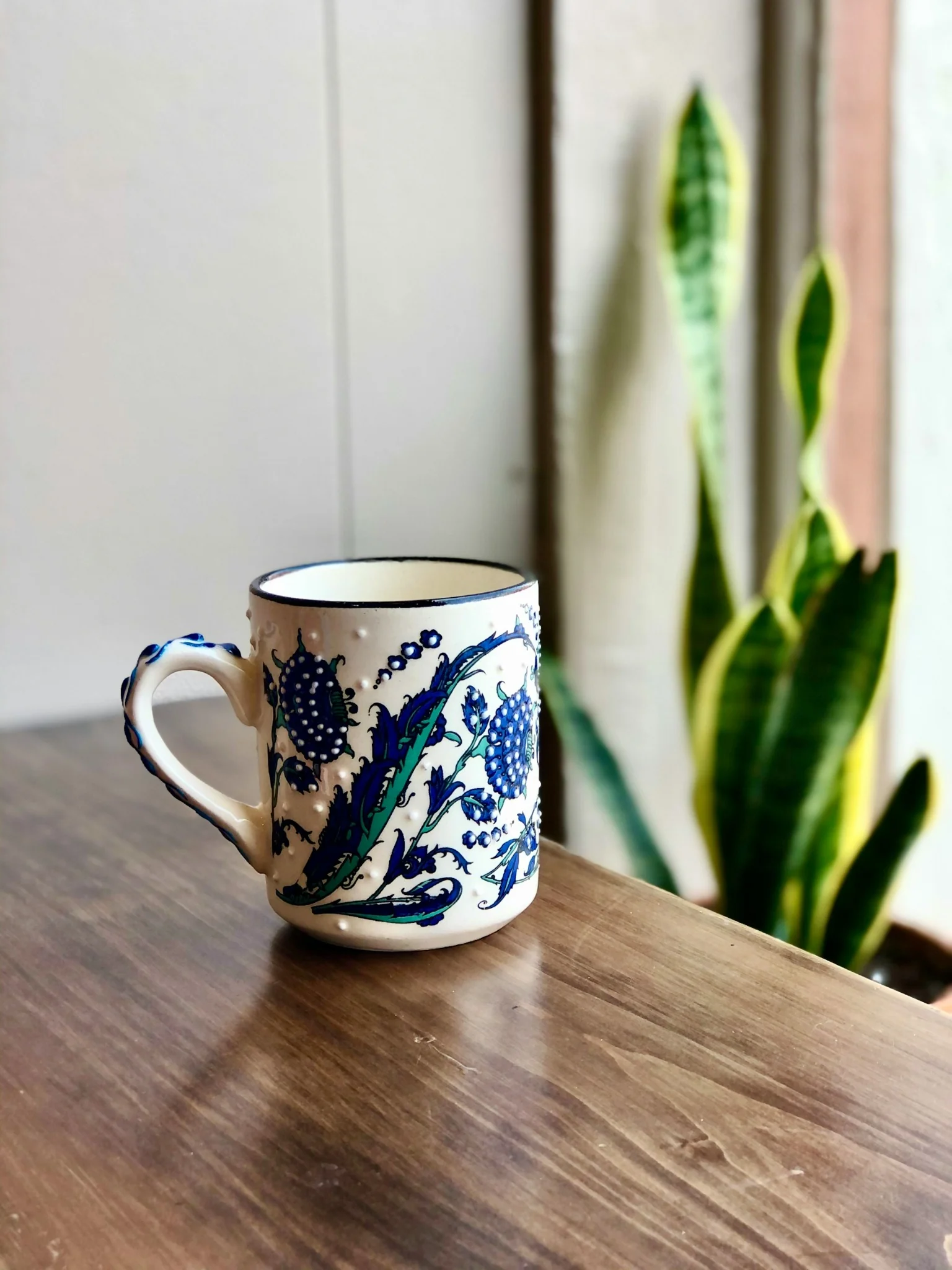 Tasse en céramique peinte à la main avec motifs bleus sur une table en bois.