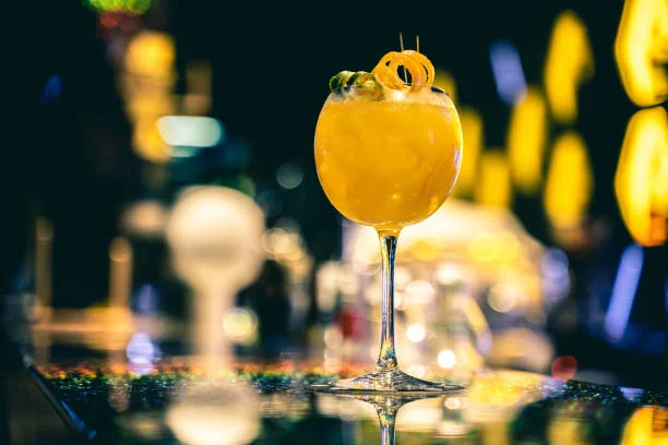 cocktail jaune servi dans un verre à pied sur un bar lumineux à dijon lors d’un evjf avant de découvrir les 10 bars pour sortir à dijon pendant un evjf
