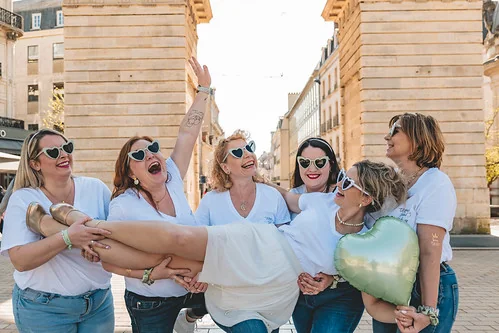 six femmes rient et soulèvent une amie dans une rue de dijon pendant un evjf avant d’aller découvrir les 10 bars pour sortir à dijon pendant un evjf