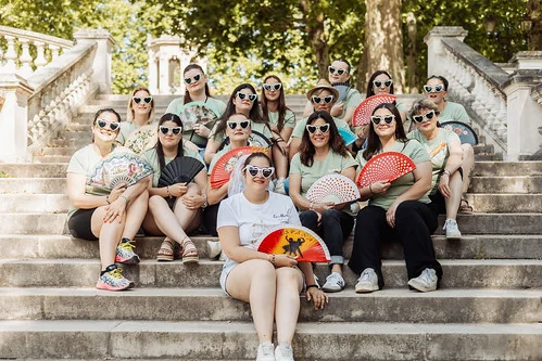 Groupe d’amies assises sur les marches d’un parc à Dijon tenant des éventails, illustrant l’article 10 bonnes raisons de faire un EVJF à Dijon