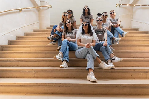 Groupe de femmes assises sur un escalier à Lille, portant des lunettes assorties pendant un EVJF, illustrant les 10 endroits où sortir à Lille pendant un EVJF.