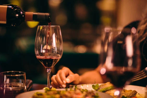 serveur versant du vin rouge dans un verre pendant un diner raffine a paris pour evjf