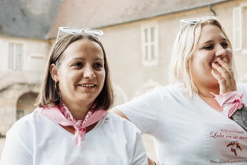 Deux amies souriantes pendant un EVJF à Dijon, portant des foulards roses dans le centre historique, illustrant les 10 endroits où sortir à Dijon pendant un EVJF.