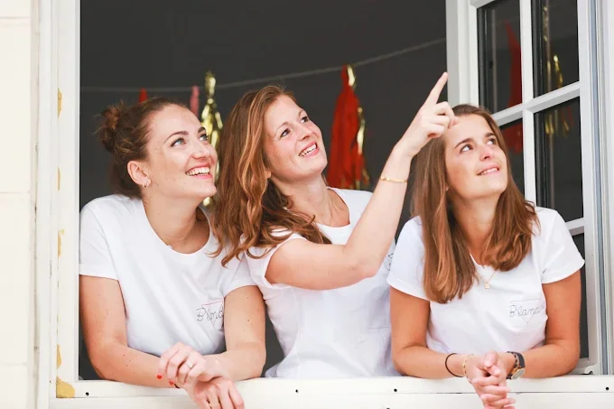 Trois amies souriantes à une fenêtre pendant un EVJF à Dijon, partageant un moment complice, illustrant les 10 endroits où sortir à Dijon pendant un EVJF.