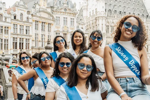 Groupe de femmes portant des écharpes bleues participant à une chasse au trésor EVJF à Bruxelles sur la Grand-Place.