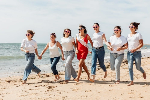 groupe de femmes courant sur la plage avec la future mariée en robe rouge
