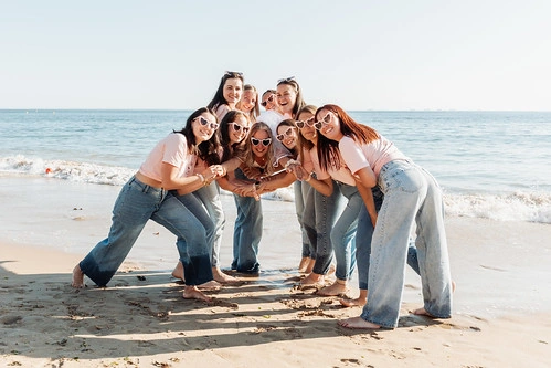 groupe de femmes souriantes en t shirt rose et jean posant sur la plage