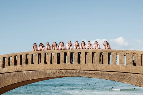 Groupe d’amies alignées sur un pont surplombant la mer avec ciel bleu et ambiance festive.