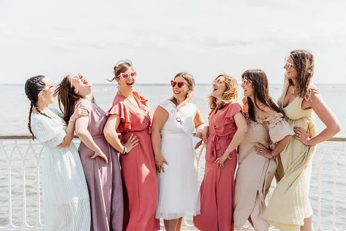 Groupe de femmes souriantes en tenue élégante face à la mer, dans une ambiance joyeuse.
