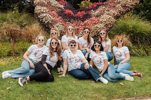 groupe de femmes assises sur l’herbe devant une sculpture florale en forme de papillon lors d’un clip vidéo evjf à caen