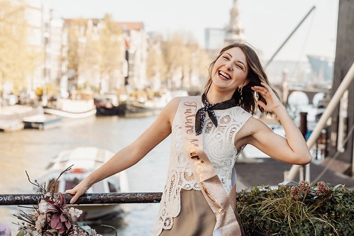 future mariée souriante portant une écharpe evjf posant près d’un canal à amsterdam