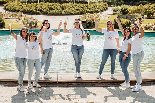 groupe de femmes portant des t shirts blancs levant leurs verres devant une fontaine lors d’un evjf à caen