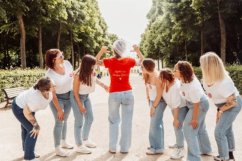 groupe de femmes riant autour de la future mariée en t shirt rouge lors d’un evjf à caen dans un parc