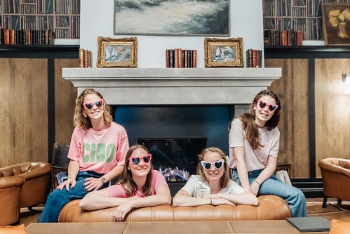 Quatre amies portant des lunettes en forme de cœur posent ensemble dans un salon cosy pendant un escape game EVJF à Paris