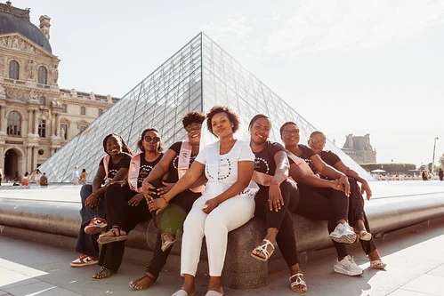 Groupe de femmes souriantes posant ensemble devant la pyramide du Louvre 