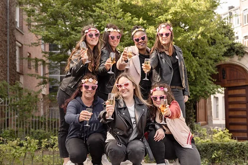 Groupe de femmes souriantes portant des lunettes en forme de cœur lors d’un EVJF à Lille, levant leurs verres en extérieur.