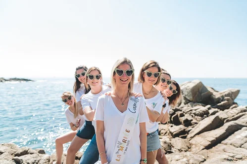 Groupe d’amies souriantes posant sur les rochers au bord de la mer à Lloret de Mar pendant un EVJF ensoleillé.
