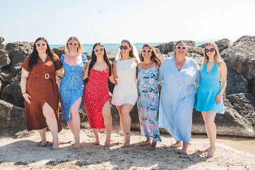 Groupe de femmes souriantes en robes colorées posant sur la plage à Palma pendant un EVJF en bord de mer.