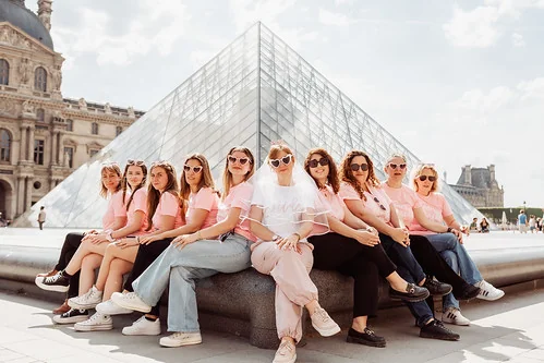 groupe de femmes en t-shirts roses posant devant la pyramide du louvre pendant un evjf à paris