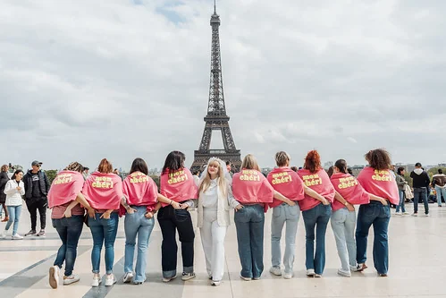 groupe de femmes portant des capes roses posant devant la tour eiffel pendant un evjf à paris