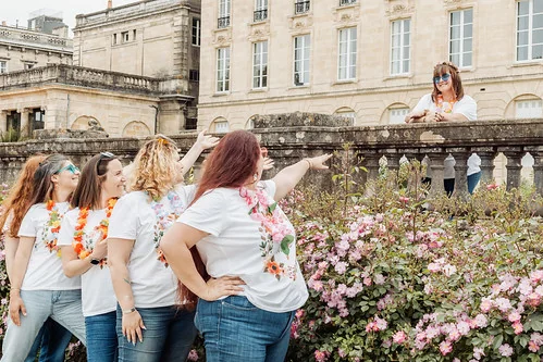 groupe de femmes en t shirt blanc riant et pointant vers une amie sur une terrasse fleurie a bordeaux pendant un evjf