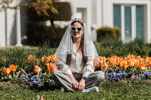 femme assise dans un jardin fleuri portant un voile et des lunettes coeur pour un evjf à annecy