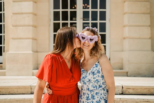 deux amies souriantes lors d un evjf a bordeaux l une en robe rouge embrassant l autre portant des lunettes en forme de coeur