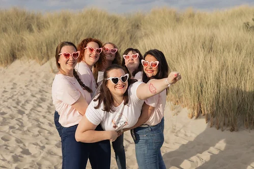 groupe de femmes en t shirt rose portant des lunettes coeur posant sur la plage du touquet pendant un evjf et des gages et defis