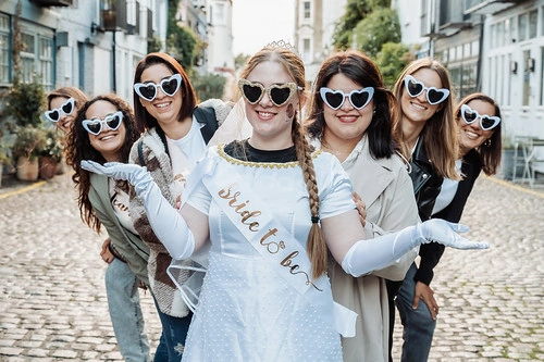 groupe de femmes celebrant un evjf a londres dans une rue typique en accompagnant la mariee avec leurs lunettes coeur, gages et defis evjf londres