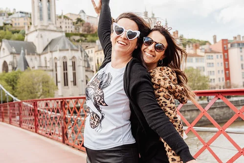 deux femmes souriantes posant sur une passerelle a lyon pendant un evjf avec vue sur la ville
