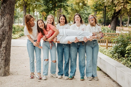 groupe de femmes riant et portant la mariee lors d’un evjf a reims pendant des gages et defis dans un parc verdoyant