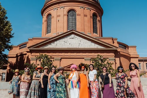groupe de femmes en robes colorees posant devant un monument en brique a toulouse pendant un evjf avec gages et defis