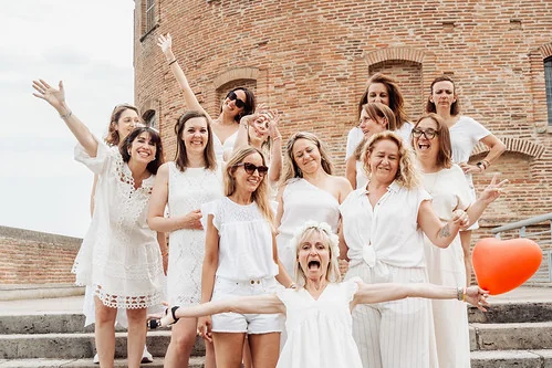 groupe de femmes en tenue blanche celebrant un evjf a toulouse devant un batiment en brique pendant les gages et defis