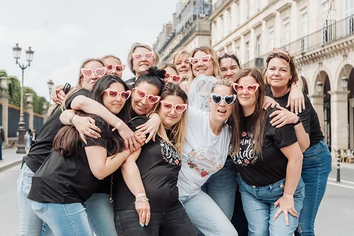 groupe de femmes souriantes portant des lunettes en forme de cœur posant dans une rue de paris pendant un evjf