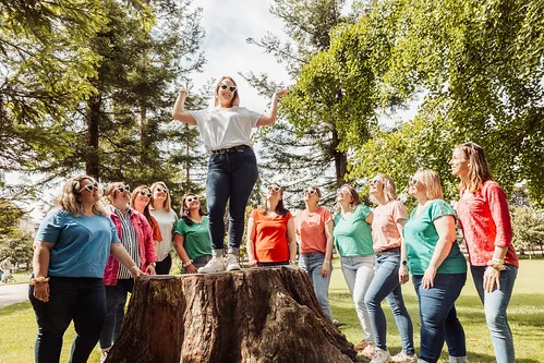 future mariee debout sur une souche entourée de ses amies pendant un koh lanta evjf a bordeaux dans un parc ensoleille