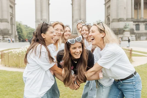 Groupe de femmes riant ensemble lors d’une activité Koh Lanta EVJF à Bruxelles, dans un parc près des arches du Cinquantenaire.