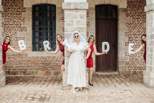 future mariee en robe blanche tenant le mot bride entouree de ses amies en robe rouge pendant un evjf a lille