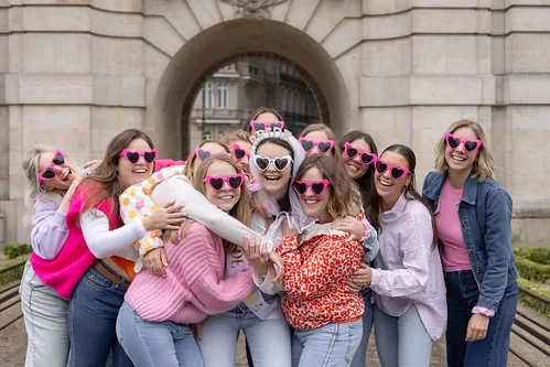 groupe de femmes souriantes portant des lunettes roses en forme de cœur enlacées pendant un evjf à lille devant un monument