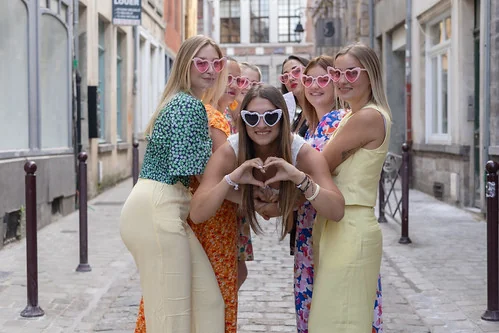 groupe de femmes souriantes portant des lunettes roses en forme de cœur posant dans une rue du vieux lille pendant un evjf