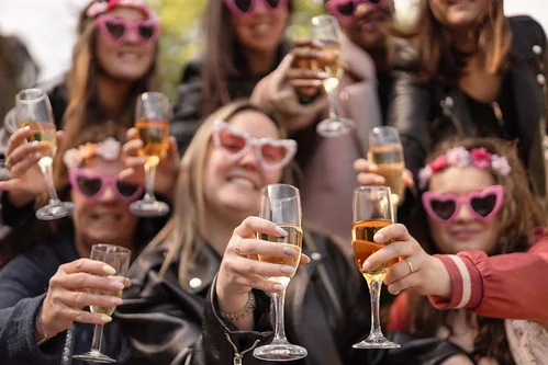 groupe de femmes portant des lunettes roses en forme de cœur trinquant au champagne pendant un evjf à lille